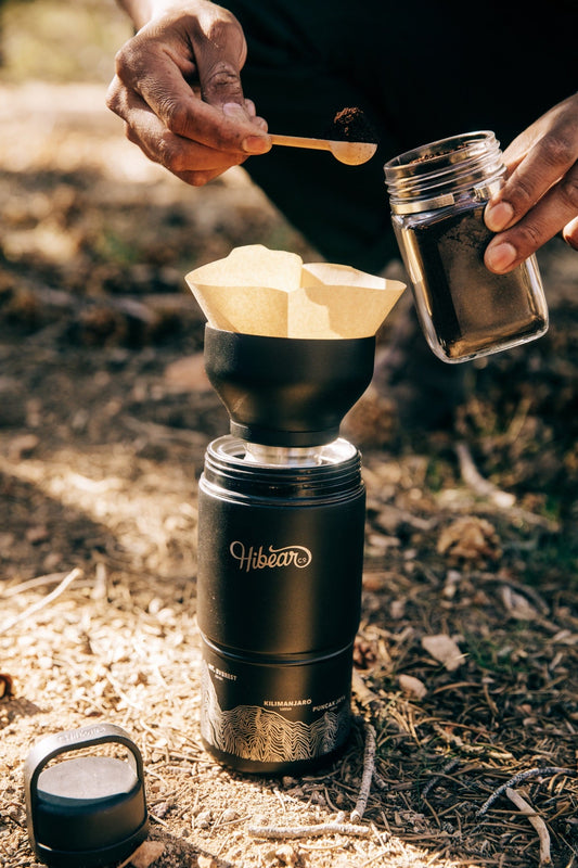 Adding ground coffee to a paper filter in the Adventure Flask Pour Over Lid outdoors.