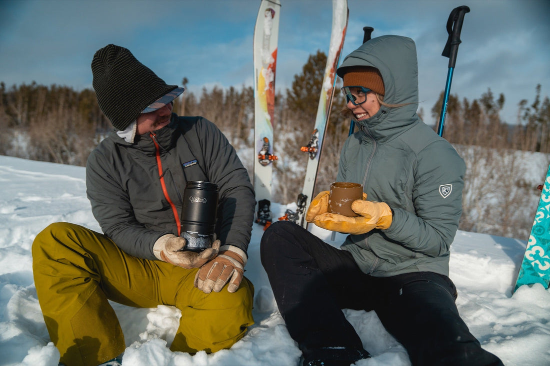 Two skiers sharing a drink with an Adventure Flask during a snowy outdoor stop.